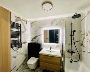 photo du projet de rénovation, montrant une salle de bains avec une majorité de marbre blanc associé à un coffrage en marbre noir , un meuble vasque et une colonne en bois et des équipements sanitaire en metal noir